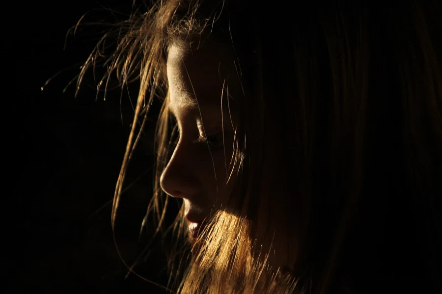 Profil de femme aux cheveux longs éclairés par une lumière rasante qui fait ressortir les mèches autour du visage