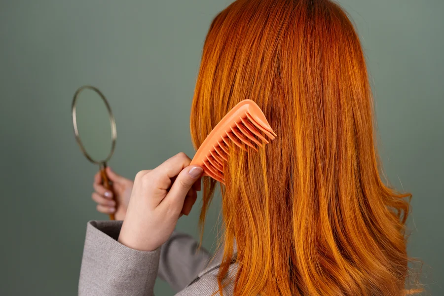 Femme aux cheveux roux démêlant ses longueurs avec un peigne à dents larges