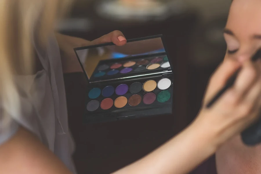 Maquilleuse qui applique un fard sur la paupière d'une femme, palette de fards ouverte