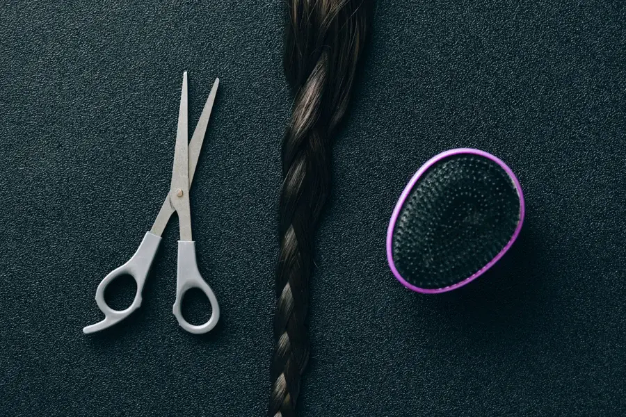 Ciseaux de coiffure posés à côté d'une mèche tressée et d'une brosse